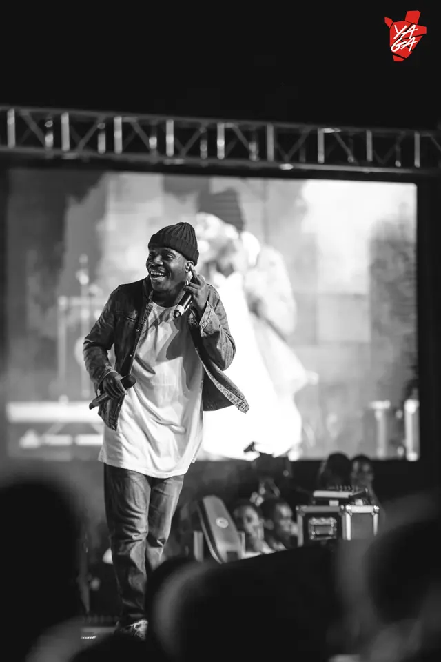 Paddy Daniel singing to a crowd beneath a large screen, black and white