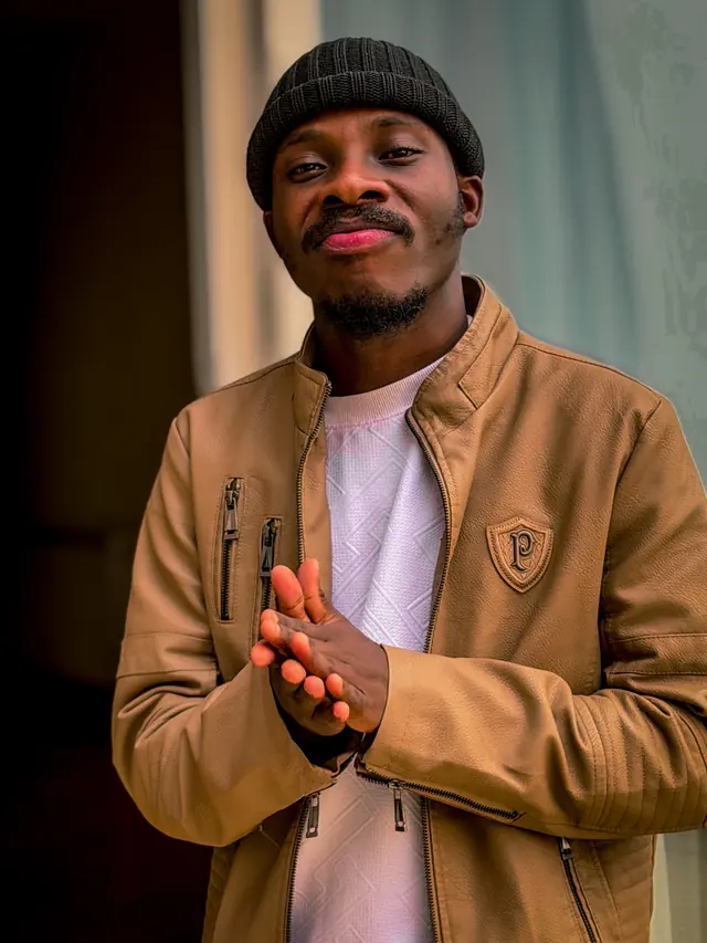 Paddy Daniel smiling in a tan jacket by a window