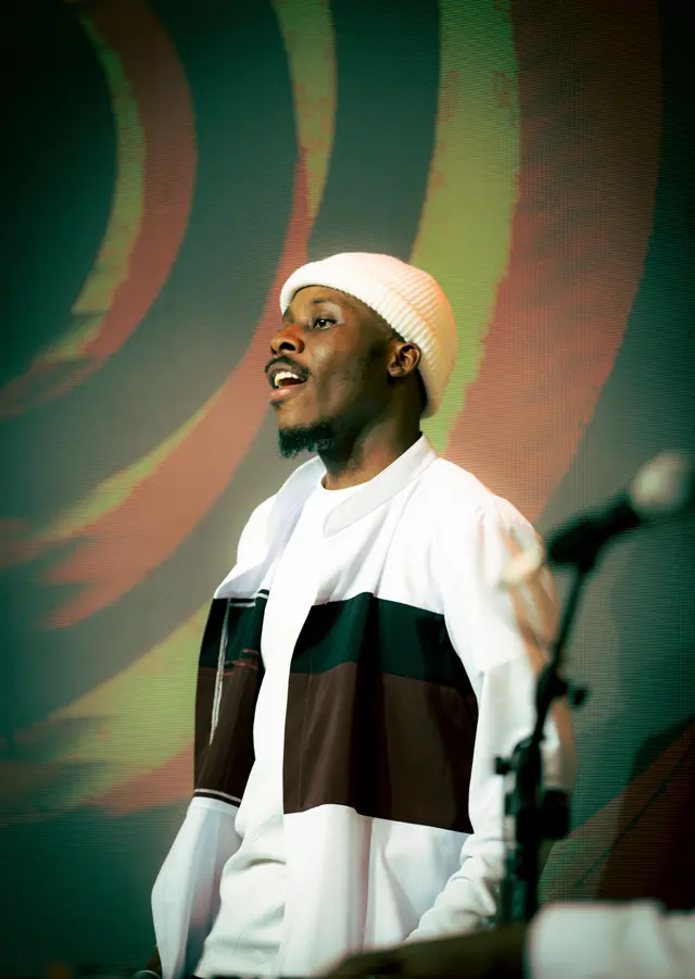 Paddy Daniel looking upward while singing in a cream beanie