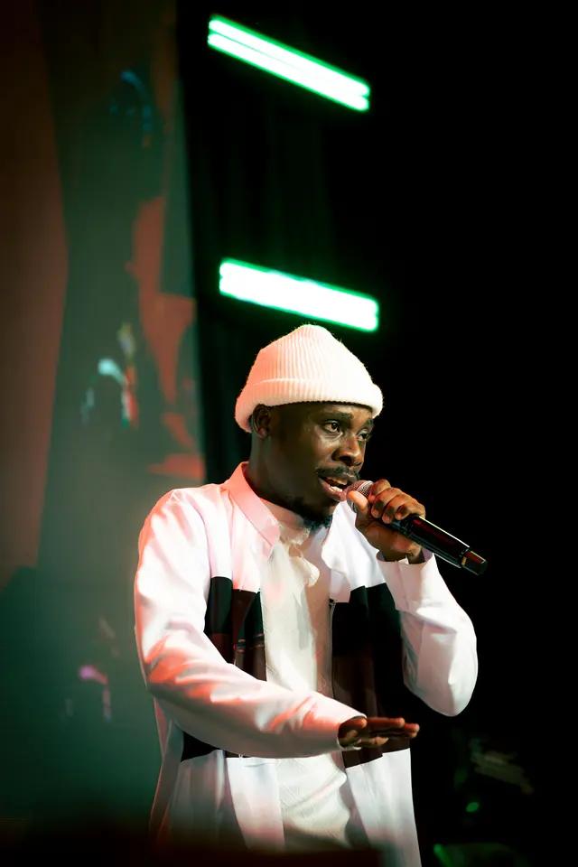 Paddy Daniel singing in a cream beanie under green light